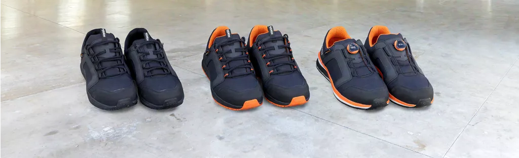 Three pairs of JALAS Tempus safety shoes with black uppers and orange details displayed on a concrete floor.