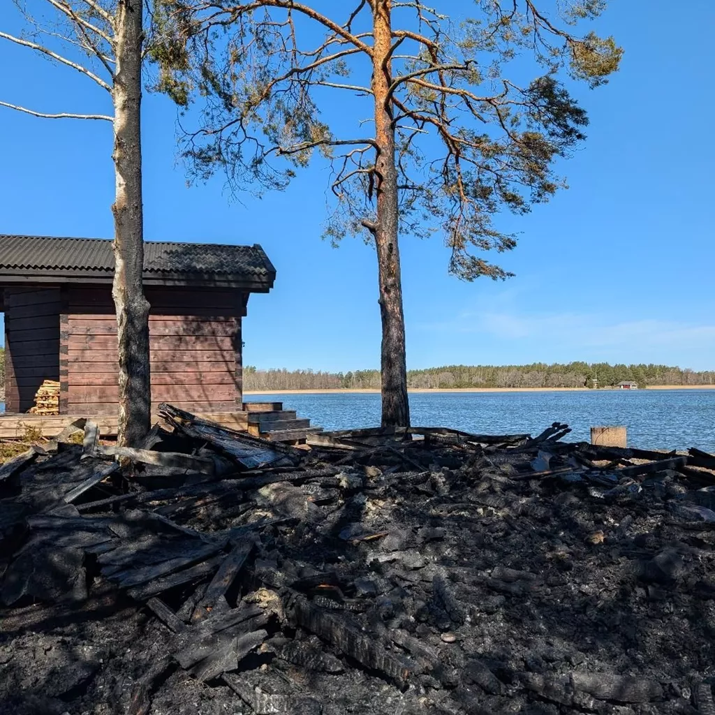 Burnt remains beside a lakeside sauna after a fire.
