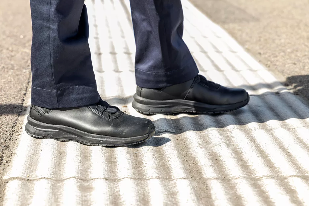 Train driver wearing black JALAS SpOc work shoes on tactile paving at a railway station platform.